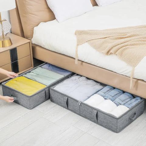Gray storage bins under a bed with folded clothes inside, in a bedroom setting.
