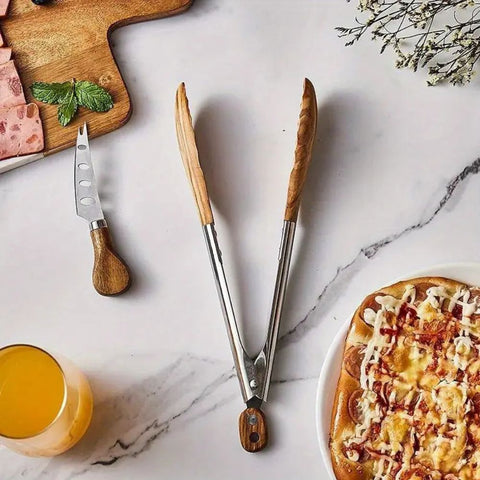 Wooden-handled tongs on a marble surface with a pizza and glass of juice.