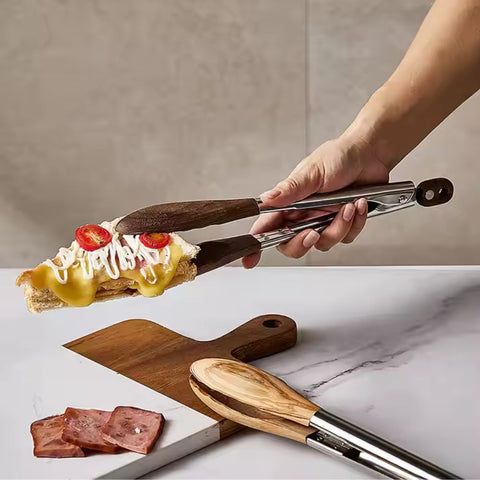 Wooden and metal tongs holding a slice of pizza with cheese and tomatoes on a marble surface.