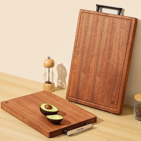Wooden cutting board with a handle on a light wooden surface, featuring an avocado and a pepper grinder.