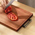 Wooden cutting board with sliced tomatoes and a knife on a light wood surface.