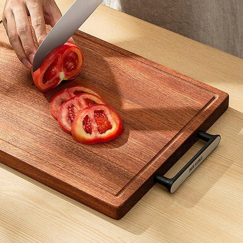 Wooden cutting board with sliced tomatoes and a knife on a light wood surface.