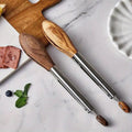 Wooden tongs with metal handles on a marble surface with food items.