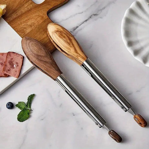 Wooden tongs with metal handles on a marble surface with food items.