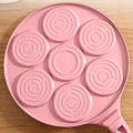  Bottom view of pink Animals Waffle and Pancake Pan showing circular heat distribution rings on wooden table