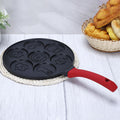 Animals waffle and pancake pan with red handle placed on braided white coaster on light wood table with bread basket nearby