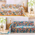 Autumn Garden Cotton Throw Blanket reversible side showing warm floral patterns on beige and rich blue backgrounds, draped over a cozy sofa in a sunlit living room