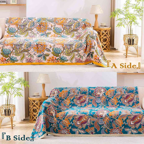 Autumn Garden Cotton Throw Blanket reversible side showing warm floral patterns on beige and rich blue backgrounds, draped over a cozy sofa in a sunlit living room