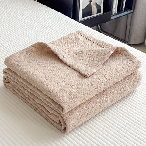 Folded beige cotton muslin quilt with minimalist geometric grid texture on bed