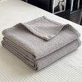 Folded gray cotton muslin quilt with minimalist geometric grid texture on bed