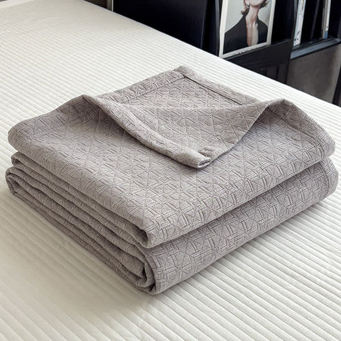 Folded gray cotton muslin quilt with minimalist geometric grid texture on bed