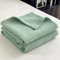 Folded green cotton muslin quilt with minimalist geometric grid texture on bed