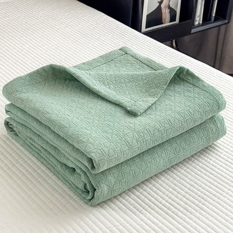 Folded green cotton muslin quilt with minimalist geometric grid texture on bed