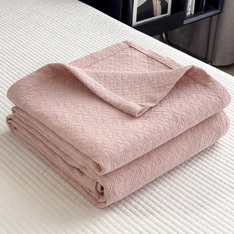 Folded pink cotton muslin quilt with minimalist geometric grid texture on bed