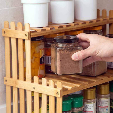 Close-up of bamboo kitchen spice shelf with hand placing spice jar on upper tier