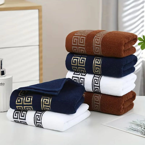 Stack of folded towels in brown, blue, and white with decorative patterns on a neutral background.