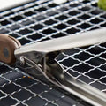 Wood and steel tongs lifting food on BBQ grill