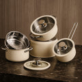 Beige nonstick cookware set with stainless steel lids on marble kitchen surface