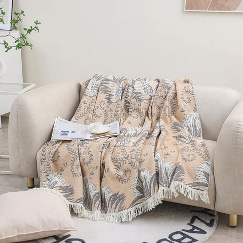 Beige cotton couch throw blanket with tassels, jacquard floral design styled on sofa with book