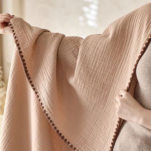 Close-up of beige crinkle cotton blanket with dark brown trim held open