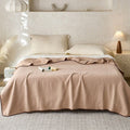 Beige crinkle cotton blanket with decorative trim draped over minimalist bed