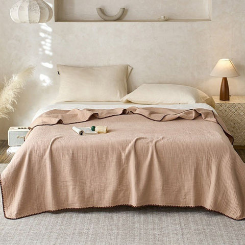 Beige crinkle cotton blanket with decorative trim draped over minimalist bed