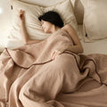 Sleeping woman wrapped in soft beige cotton muslin blanket on bed