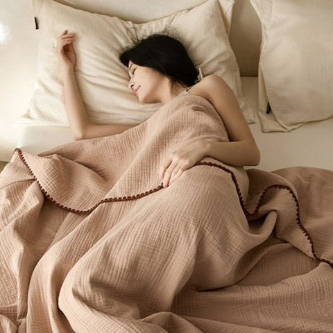 Sleeping woman wrapped in soft beige cotton muslin blanket on bed