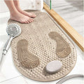 Beige textured bath mat with two footprints on a bathroom floor next to a shower head.