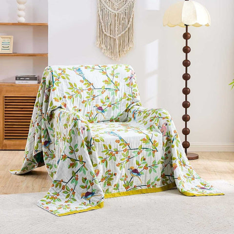  Birdsong cotton throw blanket with colorful birds and floral patterns draped on beige armchair in bright cozy room