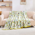 Birdsong cotton throw blanket with colorful bird and floral pattern draped over beige sofa in bright room