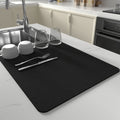 Black dish drying mat with mugs and cutlery next to sink