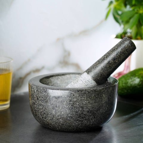 Black marble stone mortar and pestle on white surface near plant and glass