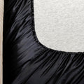 Elastic edge of black satin bed sheet stretched over mattress in twin bedding setup
