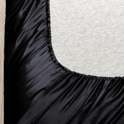 Elastic edge of black satin bed sheet stretched over mattress in twin bedding setup