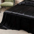 Soft black satin flat sheet draping off bed corner, showcasing silky texture and colorful bedding aesthetic.
