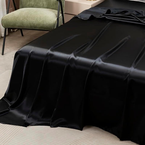Soft black satin flat sheet draping off bed corner, showcasing silky texture and colorful bedding aesthetic.