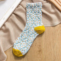 Light blue embroidered sock with white daisy floral pattern and bright yellow toe and heel, styled flat on neutral fabric.