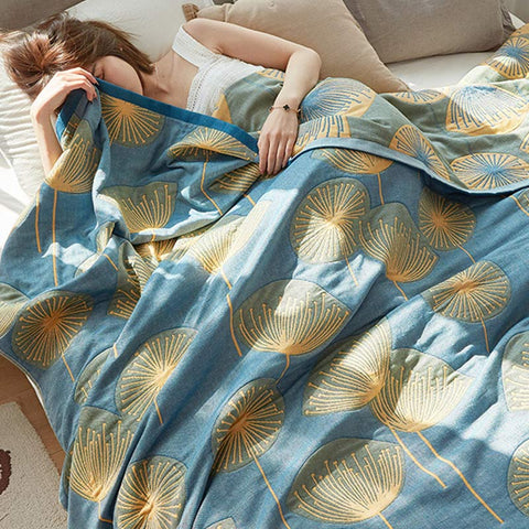 Woman resting under blue dandelion print reversible quilt – cozy and calming cotton throw