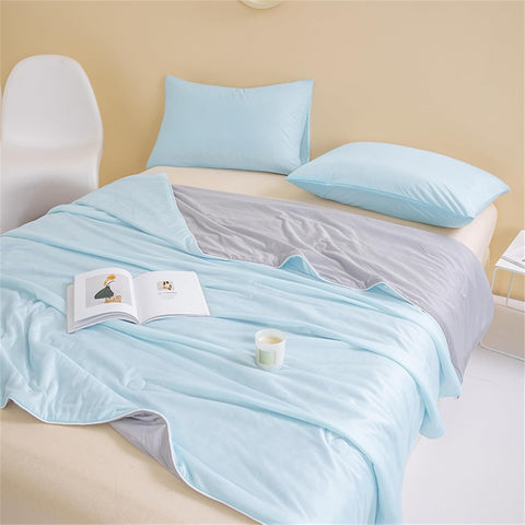 Double-layered blue and gray ice silk quilt spread on bed with pillows and natural light in serene room.