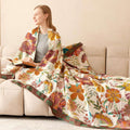 Woman wrapped in bohemian floral cotton throw blanket sitting on beige sofa reading a book in cozy setting