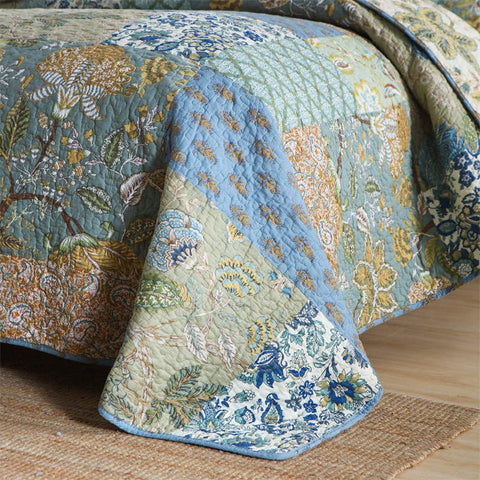 Edge of quilt with blue floral patchwork hanging from bed corner