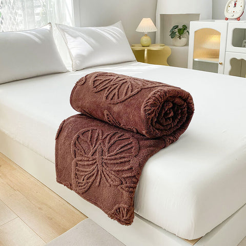 Brown butterfly embossed blanket rolled on white bed as stylish throw or warm cover