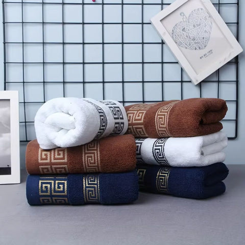 Stack of folded towels in white, brown, and blue with decorative patterns on a grid background.