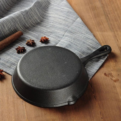 Black cast iron skillet on a wooden surface with a gray cloth and cinnamon sticks.