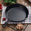 Black cast iron skillet on a wooden table with tomatoes and garlic