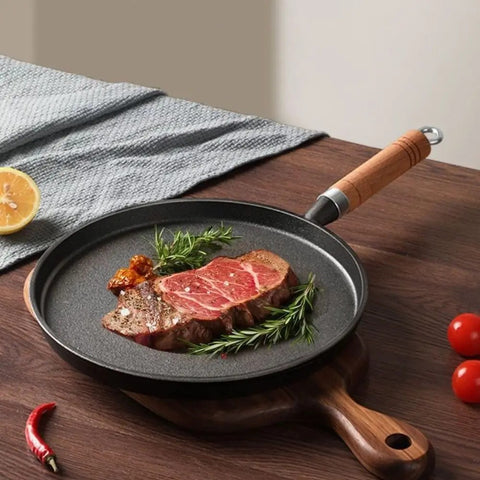 Steak on a frying pan with wooden handle on a wooden table