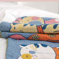 Close-up of Cat Party cotton pillowcase fabric showing detailed colorful cat illustrations on soft blue cotton material, folded on a white bed.