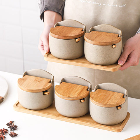 Set of ceramic containers with wooden lids on a wooden tray held by a person.