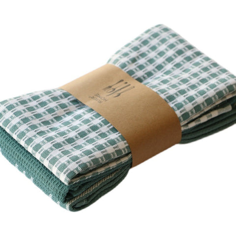 Folded green checkered cotton towel with a brown paper wrap on a white background